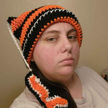 A picture of someone wearing an orange & black crochet hat. It links to a gallery of example work